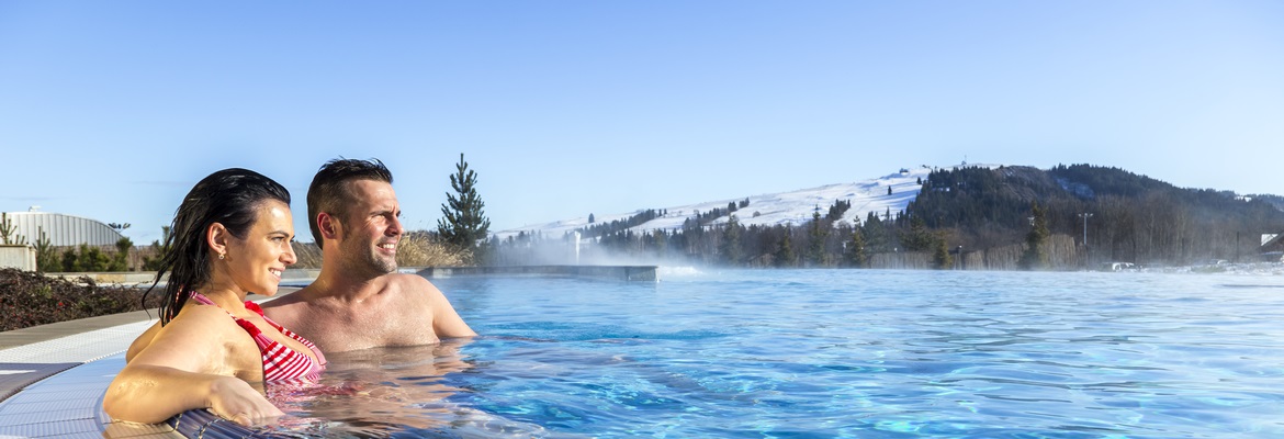 Para - kobieta i mężczyzna relaksujący się zimą w zewnętrznym basenie Term Bania w Białce Tatrzańskiej; w tle ośnieżone góry - Tatry
